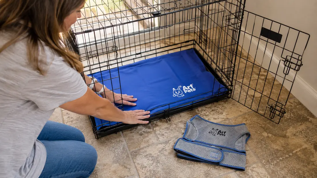 Hands unrolling the Arf Pets gel cooling mat onto a crate floor next to a folded cooling vest